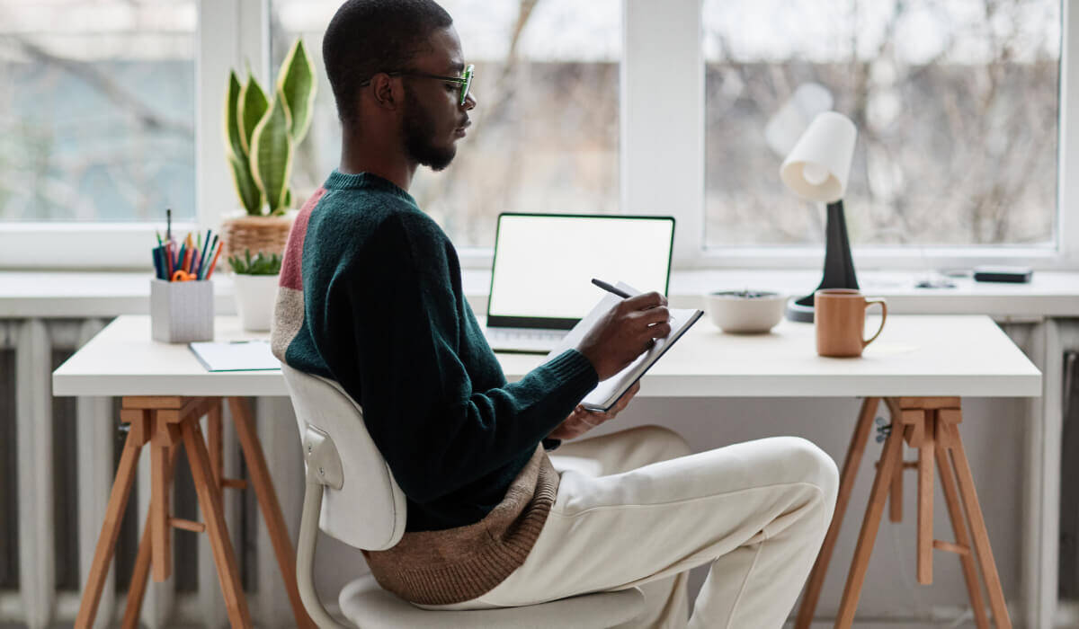A focused Black man taking notes in a serene, naturally-lit workspace, embodying the strategic planning and design optimization integral to Vaulted's HubSpot web services.