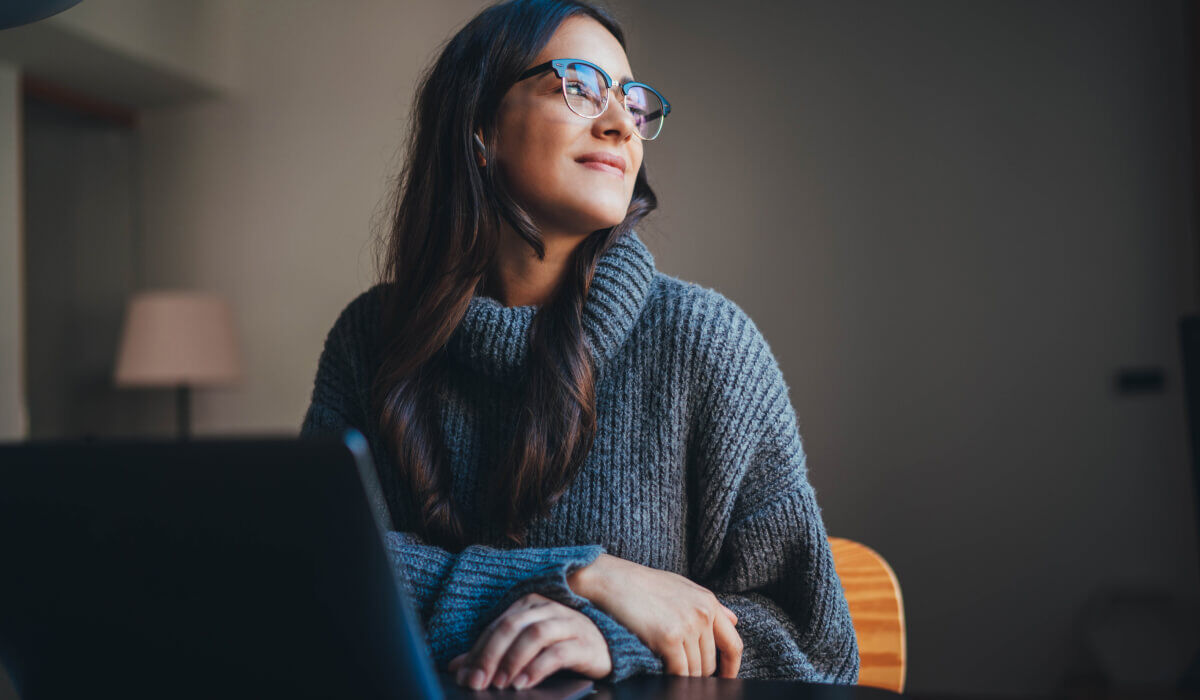 A woman in glasses and a sweater looks thoughtfully away from her laptop, illustrating the reflective planning behind Vaulted’s HubSpot web design services.