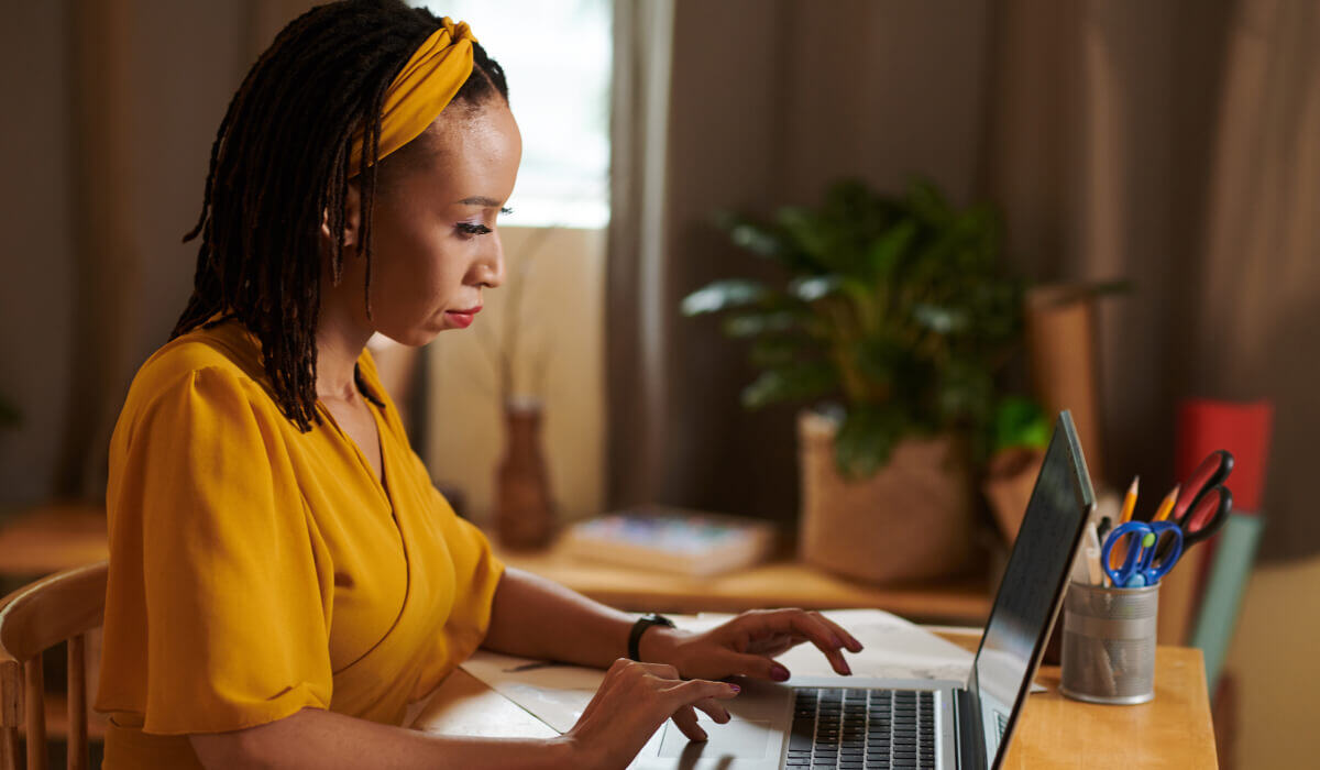 A woman in a yellow blouse concentrates on her laptop in a cozy, plant-filled office, reflecting the focused and personalized approach of Vaulted's HubSpot web design services