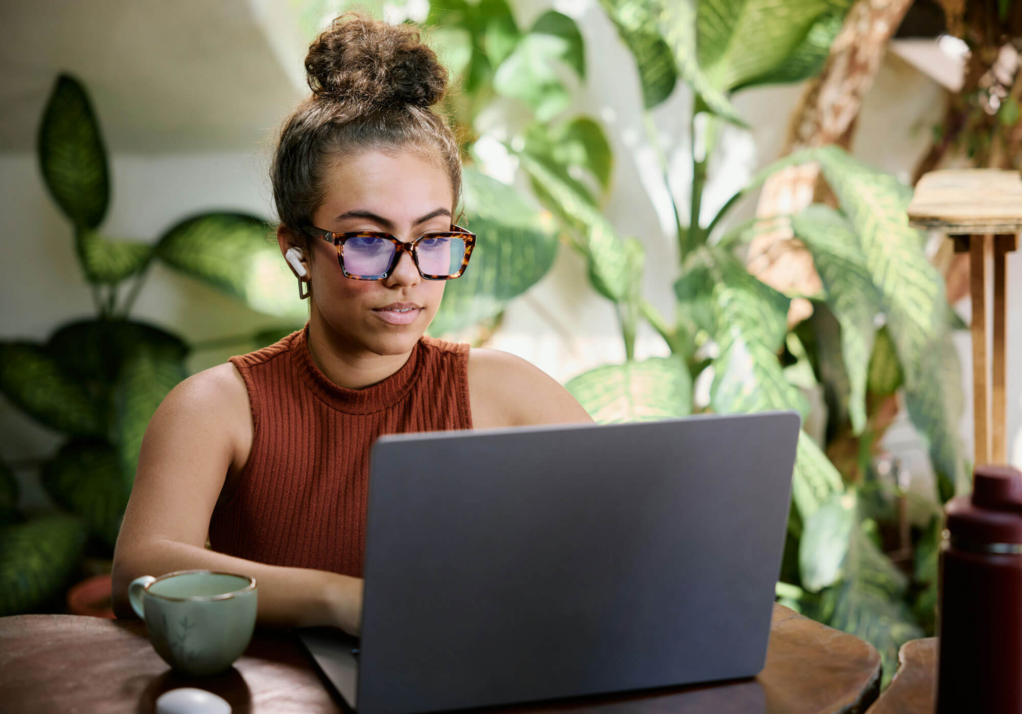 Woman researching on a laptop in a plant-filled workspace