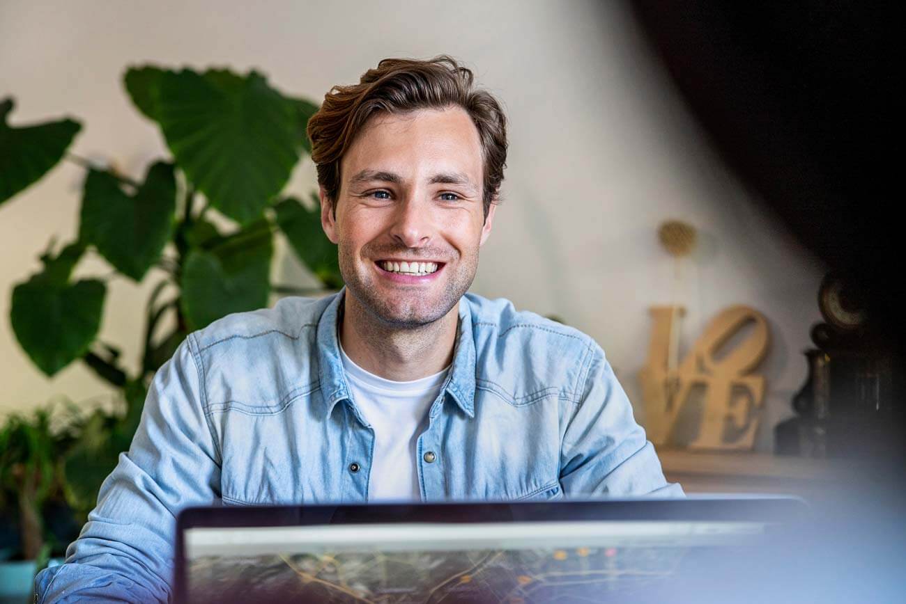 Smiling man at laptop in modern office, representing a Durham-based professional evaluating web design and brand strategy.