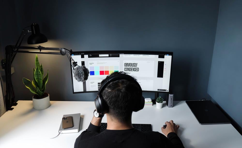 Designer wearing headphones works on branding concepts at an ultra-wide monitor, creating a cohesive brand identity for a client’s HubSpot website.