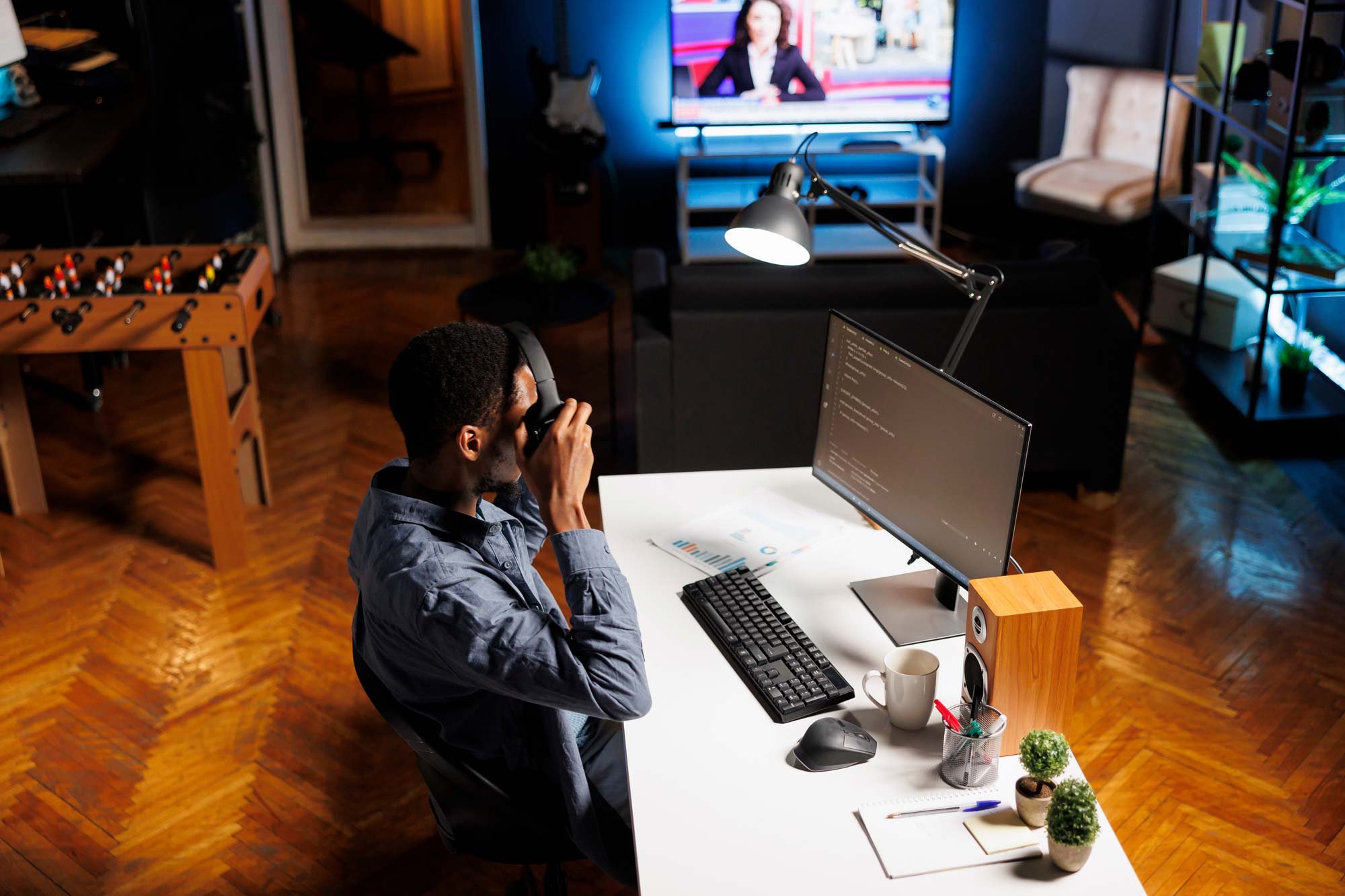 A developer in a modern workspace sits at a desk with a large monitor displaying code, putting on headphones while preparing to work—representing the focus and technical expertise of a HubSpot Agency.