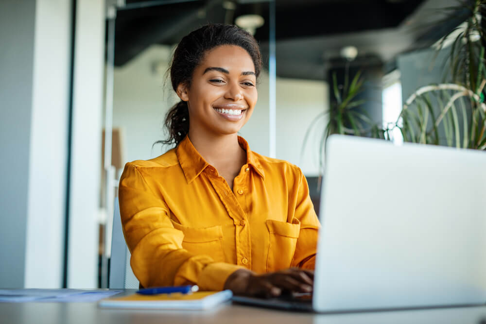 Smiling customer‑support agent working on a laptop, illustrating how AI improves efficiency and consistent service.