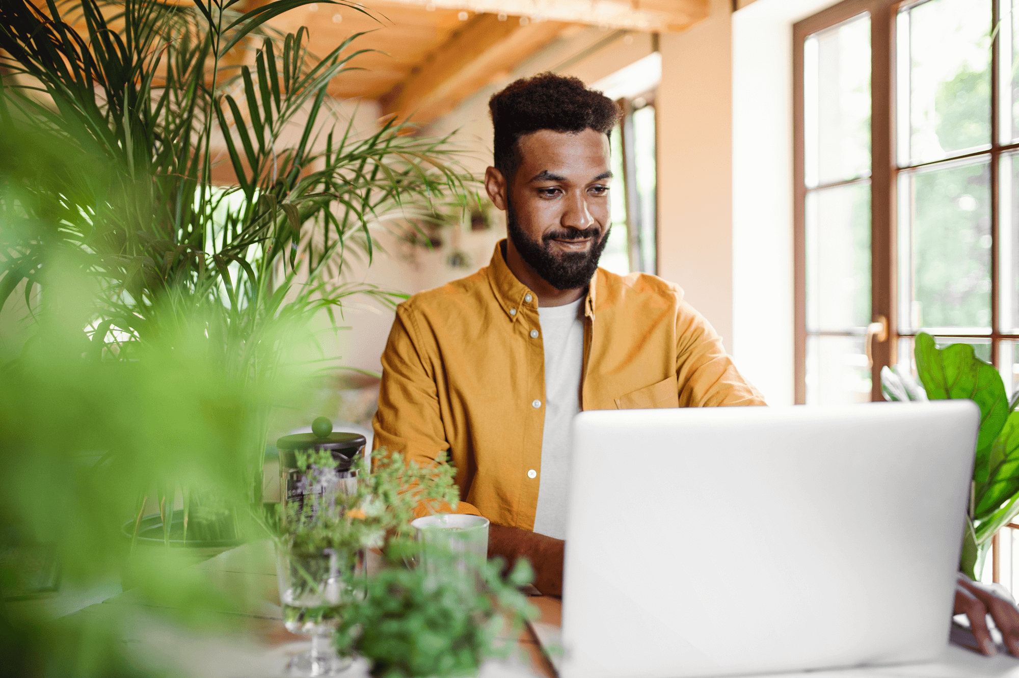 Man in a bright, plant-filled workspace using a laptop, illustrating the importance of local keyword optimization for attracting targeted customers in Raleigh.
