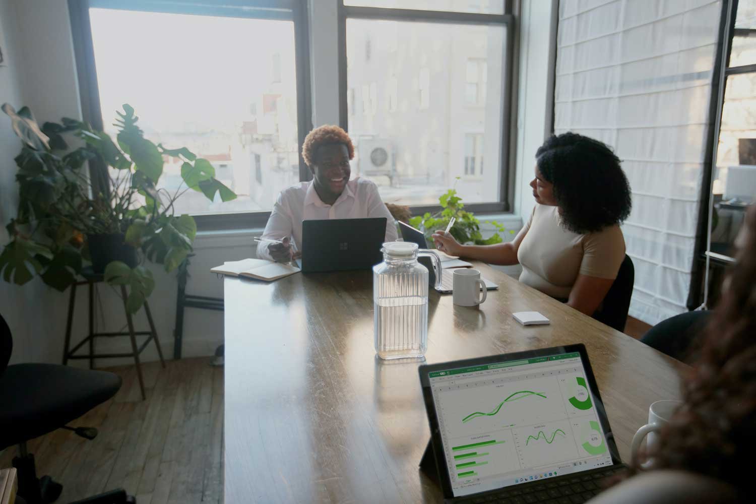 Two African American women engaged in a focused conversation while looking at a computer screen, discussing how to organize lists in HubSpot. One woman points at the screen, suggesting a specific action, while the other listens attentively, ready to implement the changes.